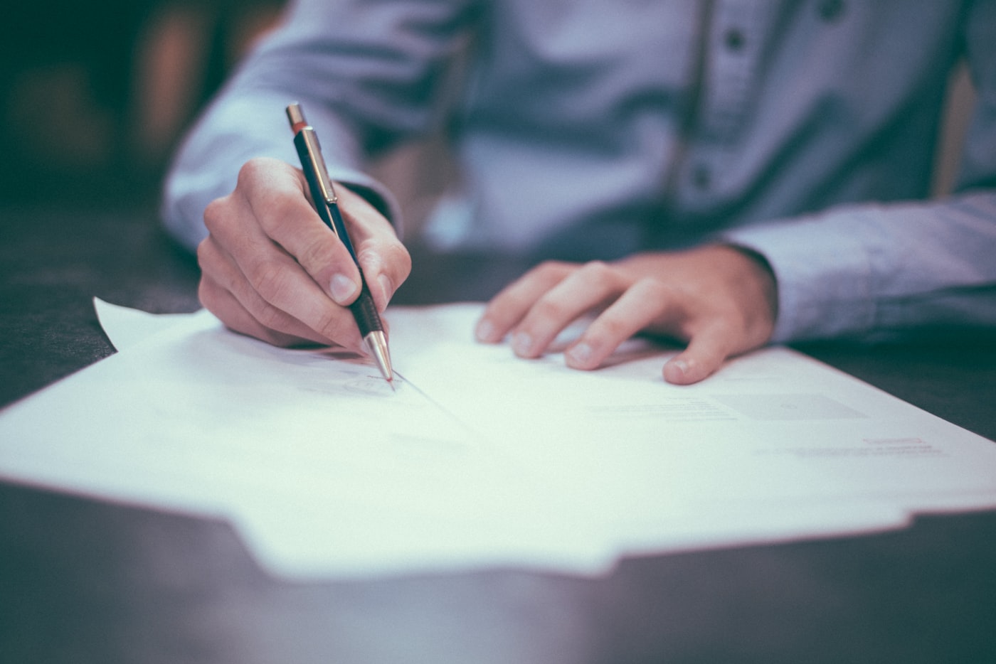 A person signing a document at a desk with a fountain pen.